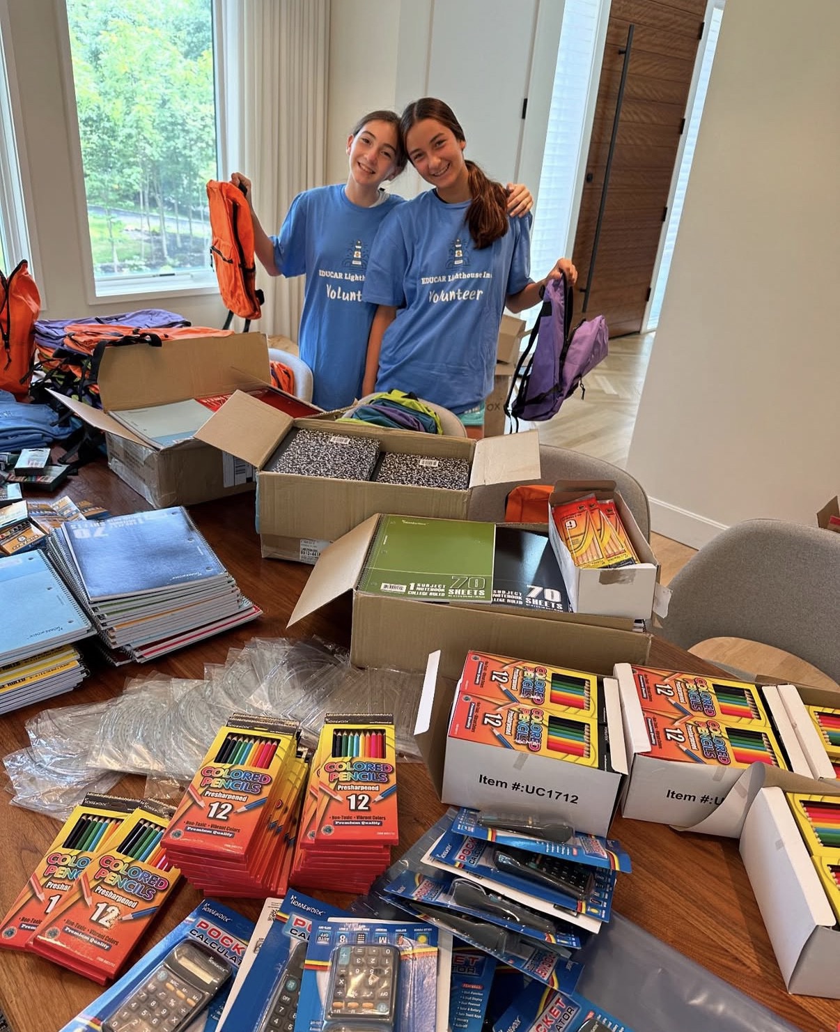 Volunteers assembling backpacks surrounded by boxes of notebooks, pencils, and calculators