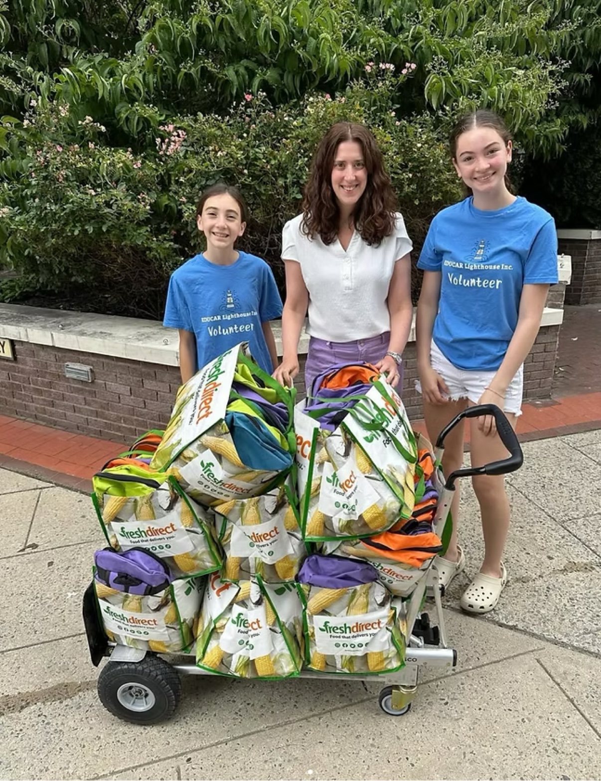 Volunteers delivering a cart full of backpacks packed with school supplies to My Sisters' Place